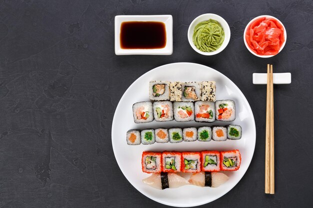 Traditionelles japanisches Restaurant. Buntes Sushi-Set serviert auf einer weißen Platte mit Stäbchen, Sojasauce, Ingwer und Wasabi. Draufsicht auf grauem Hintergrund mit Kopienraum