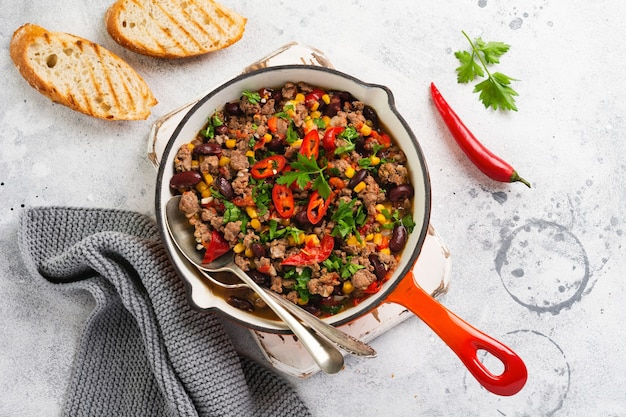 Traditionelles mexikanisches Essen - Chili con Carne in einer gusseisernen Pfanne auf hellgrauem Schiefer oder Betonoberfläche. Draufsicht mit Kopierraum.