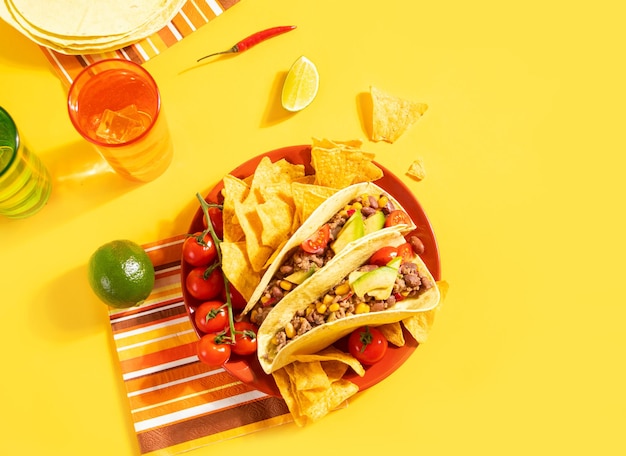 Traditionelles mexikanisches Essen Mais-Tacos mit Fleisch, Gemüse, Avocadobohnen, Mais-Salsa und Nachos, serviert mit verschiedenen Saucen und Getränken auf gelbem Hintergrund Draufsicht Große Familienfeiern