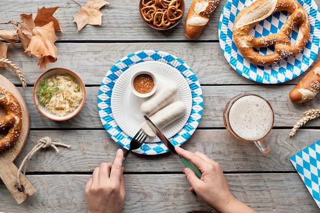 Traditionelles Oktoberfest-Essen, flach auf Holztisch mit blauen und weißen Papierdekorationen.