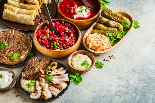 Traditionelles russisches Küchekonzept. Borschtsch, geliertes Fleisch, Schmalz, Crepes, Salatvinaigrette und Sauerkraut, grauer Hintergrund.