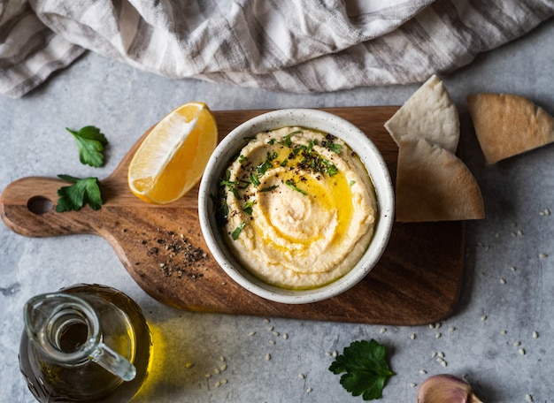 Traditionelles selbst gemachtes Kichererbsenhummus, nieselte mit Olivenöl und frischer Petersilie und neuen Pittabrotscheiben auf hölzernem Schneidebrett