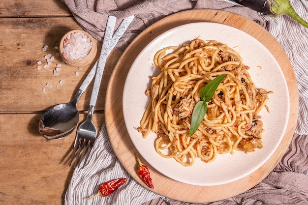 Traditionelles sizilianisches Nudelgericht aus sautierten Auberginen mit Tomatensauce. Essen auf einer Keramikplatte serviert, italienische Küche, modernes hartes Licht, dunkler Schatten. Holztisch Hintergrund, Ansicht von oben