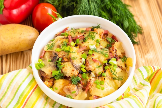 Traditionelles Tartiflette mit Speck, Kräutern und Gemüse über Holztisch. Draufsicht.