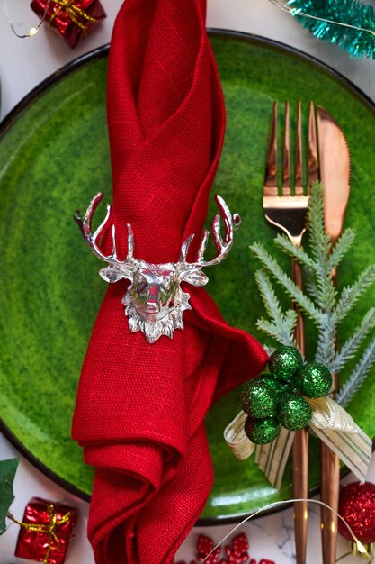 Traditionelles Weihnachtsgedeck aus nächster Nähe. Goldenes Besteck, Leinenserviette mit Hirschring, Fichtenzweige. Feiertage Hintergrund. Flache Lage, Draufsicht, selektiver Fokus.