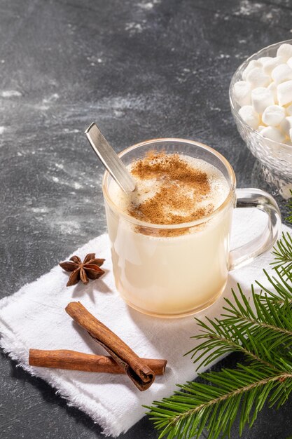 Traditionelles Weihnachtsgetränk hausgemachter Eierlikör mit Zimt, Löffel im Glas auf weißer Serviette auf Schwarz.