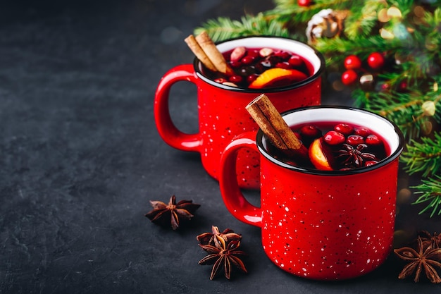 Traditionelles Weihnachtsglühweingetränk mit Preiselbeerorangenscheiben und Gewürzen in roten Bechern auf dunklem Steinhintergrund kopieren Raum