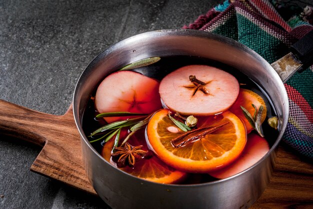 Traditionelles Winter- und Weihnachtsgetränk, heißes Getränk des Glühweins mit Zitrusfrucht, Apfel und Gewürzen in der Aluminiumkasserolle auf schwarzer Steintabelle. kopieren sie platz