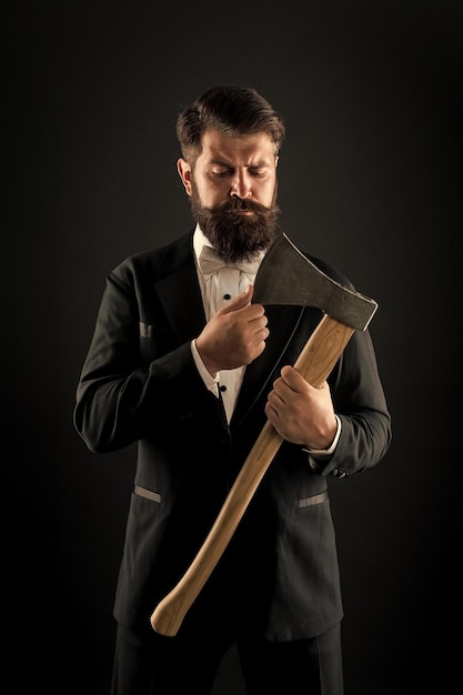 Foto trae más estilo para el rostro barbudo hombre barbudo mantiene el hacha hipster barbudo en estilo de esmoquin clásico novio sin afeitar con rostro barbudo salón de afeitar barbería