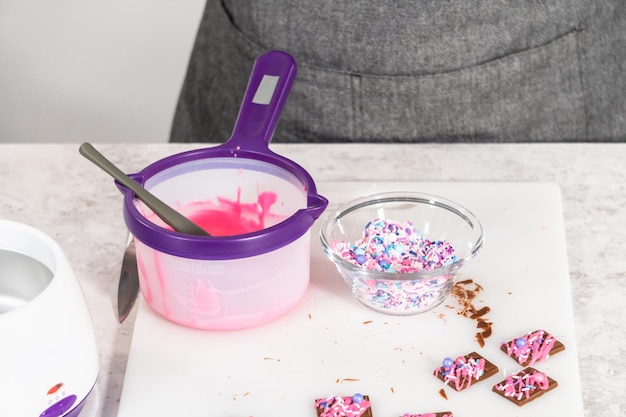 Träufeln Sie geschmolzene rosa Schokolade auf die Mini-Pralinen und streuen Sie einige bunte Streusel darüber.