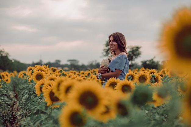 Träumende junge Frau im blauen Kleid, die einen Hut in einem Feld von Sonnenblumen im Sommer hält, Blick von ihrer Seite. Zur Seite schauen. Speicherplatz kopieren