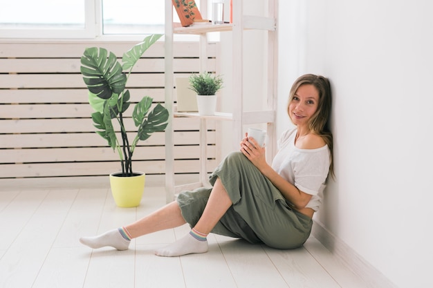 Träumendes Mädchen, das zu Hause auf dem Boden sitzt und Tee aus der Tasse trinkt