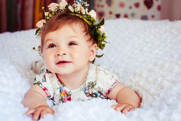 Träumerisches kleines Mädchen mit Rosenkranz auf goldenem Haar liegt auf flauschiger Decke