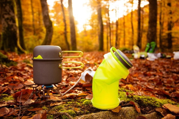 Tragbarer Gasheizer und Pfanne zum Kochen im Freien beim Camping Zusammenklappbare Flaschen, um Platz im Rucksack zu sparen Herbstwald im Hintergrund verschwommen Geräte zum einfachen Wandern und Reisen