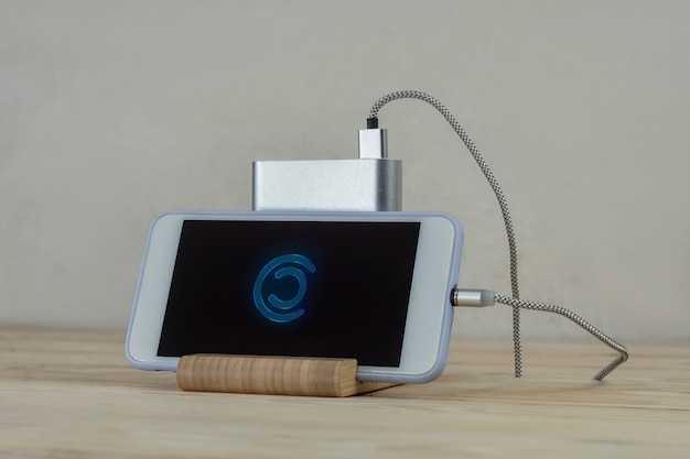 Tragbares Ladegerät lädt ein Smartphone auf einem Holztisch. Handymodell mit dunklem Bildschirm und Powerbank.