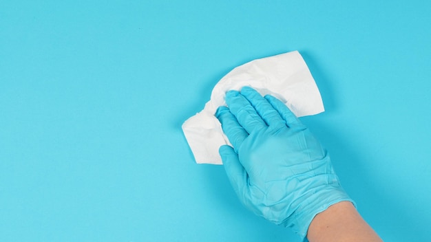 Tragen Sie einen medizinischen Handschuh und wischen Sie Seidenpapier auf blauem Hintergrund ab Studiobild