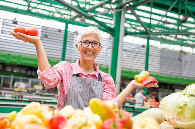 Tragende Gläser der schönen älteren Frau verkauft Pfeffer auf Markt