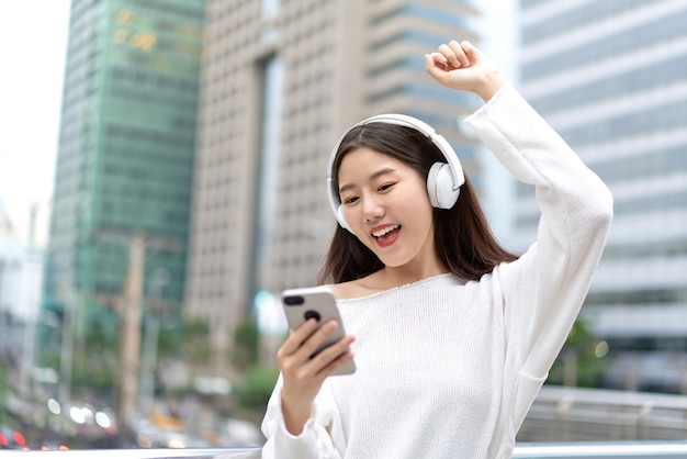 Tragende Kopfhörer des asiatischen Mädchens, die online Musik vom Smartphone hören