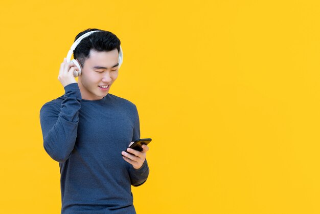 Tragende kopfhörer des glücklichen asiatischen mannes, die musik vom smarrt telefon strömen hören