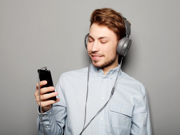 Tragende Kopfhörer des jungen Mannes und Halten des Handys