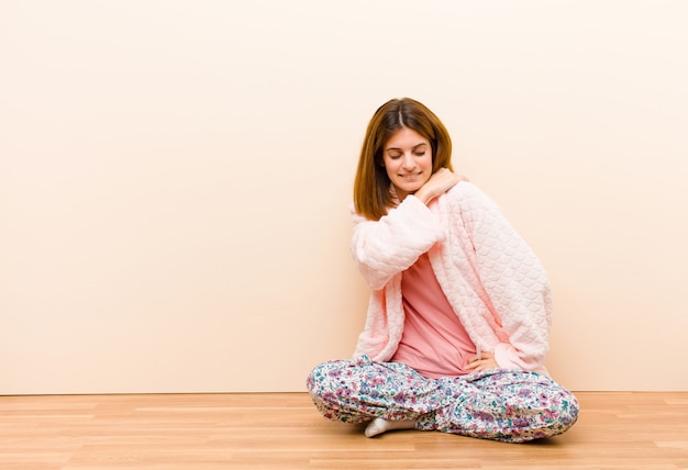 Tragende Pyjamas der jungen Frau, die zu Hause sitzen, fühlend müde, betont, besorgt, frustriert und deprimiert und leiden mit Rücken- oder Nackenschmerzen