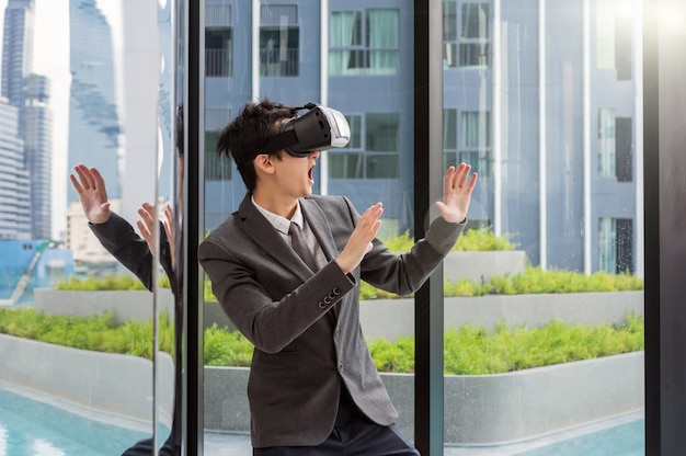 Tragende virtuelle Realität des asiatischen Mannes mit Anzug am modernen Gebäude