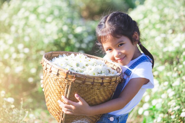 Tragender Korb des netten asiatischen Kindermädchens der schönen Blume auf dem Blumengebiet mit Glück