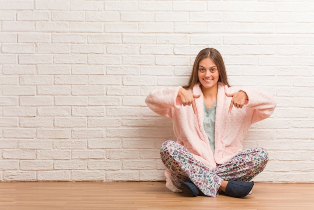 Tragender Pyjama der jungen Frau, der auf die Unterseite mit den Fingern zeigt