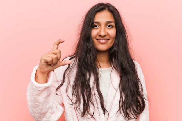 Tragender Pyjama der jungen indischen Frau, der etwas wenig mit den Zeigefingern, Lächeln und überzeugt hält.