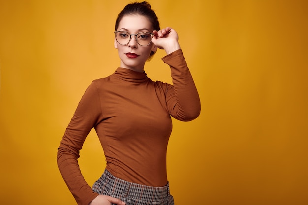Tragender Rollkragenpullover und Gläser der Mode Brunette-Frau auf gelbem Hintergrund
