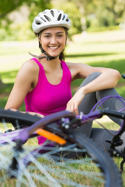 Tragender Sturzhelm der glücklichen Frau mit Fahrrad im Park