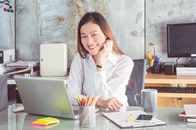 Tragendes weißes Hemd der jungen asiatischen schönen Geschäftsfrau, das im Arbeitsbüro lächelt