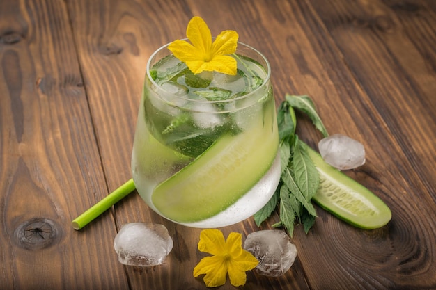 Un trago de agua con pepinos y flores de pepino sobre un fondo de madera