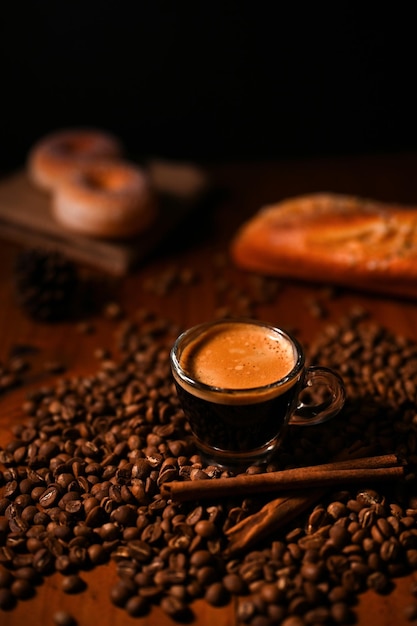 Un trago de café, un trago de espresso en una taza de vidrio sobre una mesa de madera con granos de café arábica