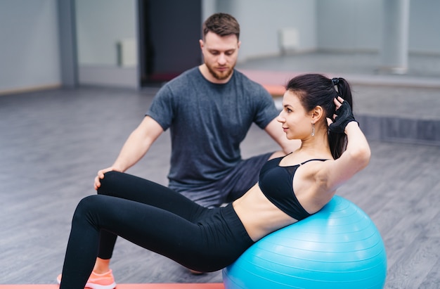 Trainer hilft Kunden beim Training auf Gymnastikball im Fitnessstudio.