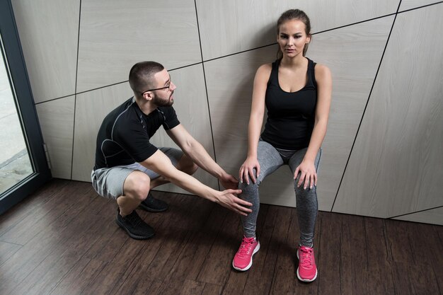 Trainer hilft Mädchen im Fitnessstudio auf Beinen