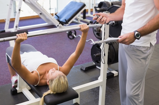 Foto trainer mit klemmbrett außer der frau, die barbell in der turnhalle anhebt