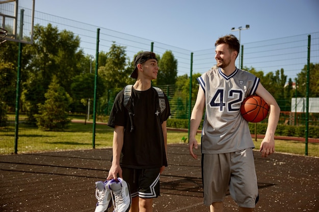 Trainer und Teenager reden nach dem Basketballtraining auf dem Straßenplatz. Hobby, aktiver Lebensstil, Sportaktivität