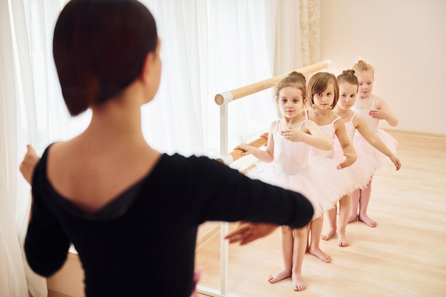 Trainer unterrichtet Kinder kleine Ballerinas, die sich auf die Aufführung vorbereiten, indem sie Tanzbewegungen üben