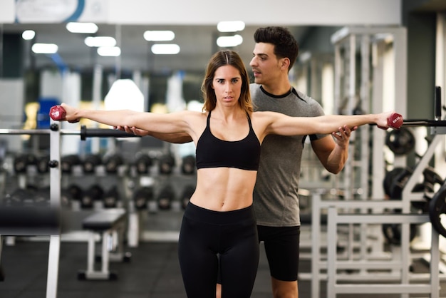 Trainerin, die eine Frau beim Training im Fitnessstudio unterstützt