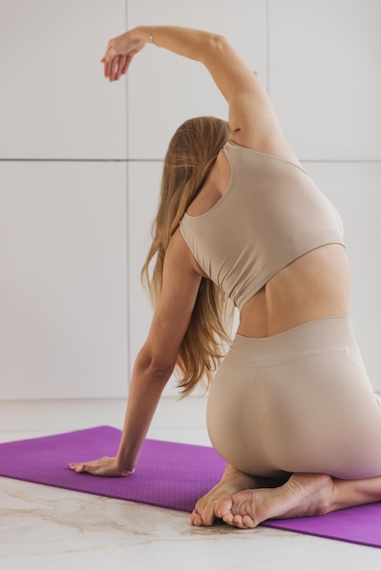 Trainieren Sie zu Hause Fröhliches tausendjähriges Mädchen, das in einem hellen Raum mit Panoramafenstern Ausfallschritte auf einer Yogamatte macht