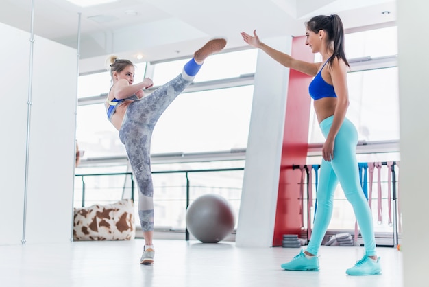 Training der jungen kaukasischen Frau mit einem Personal Trainer im Fitnessstudio, das hohe Seitentritte übt.