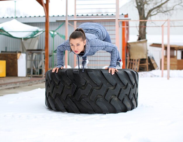 Training der jungen muskulösen Frau auf schwerem Reifen, draußen