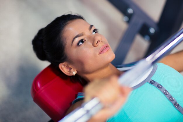 Training der jungen Sportfrau mit Langhantel auf der Bank im Fitness-Studio