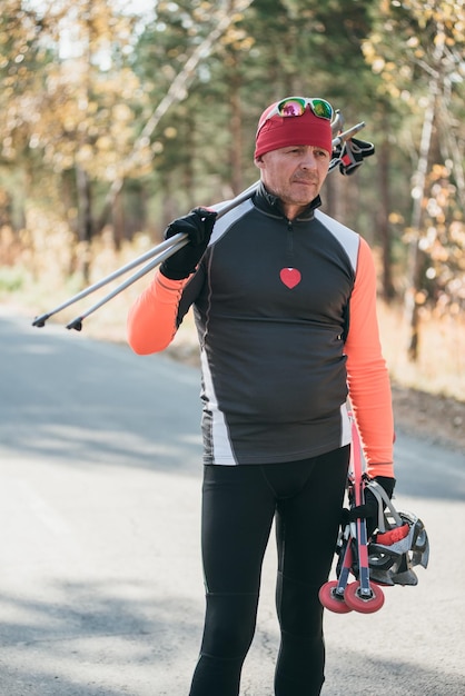 Training eines Athleten auf den Rollschuhen Biathlonfahrt auf den Rollskiern mit Skistöcken im Helm Herbsttraining Rollsport Der Athlet geht und hält Sportgeräte in der Hand