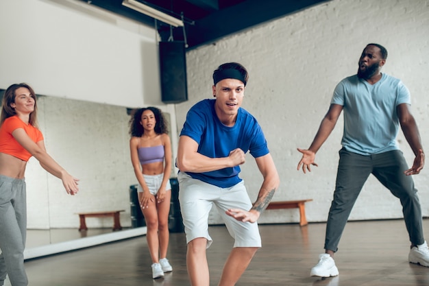 Training, Stimmung. Fröhlicher Kerl mit Tätowierung auf seinem Arm tanzt mit Freunden beim Tanztraining