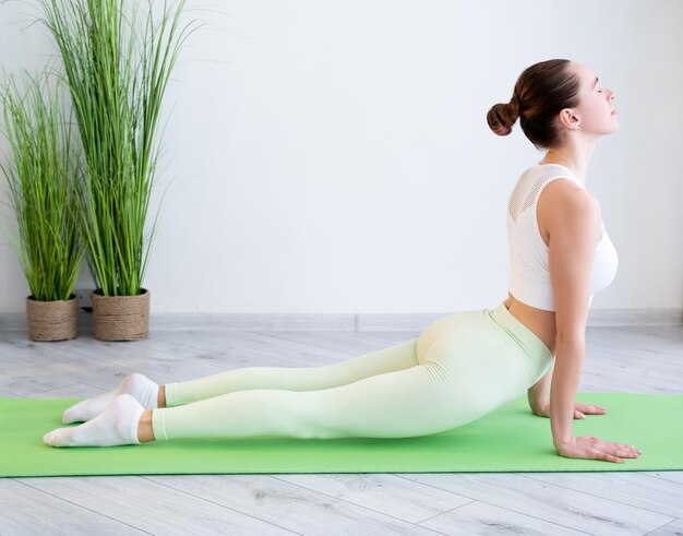 Training zu Hause Pilates-Übung Körperliche Aktivität Fitte sportliche Frau in Sportbekleidung, die Gymnastik praktiziert, die sich auf einer Yogamatte im Fitnessstudio drinnen ausdehnt