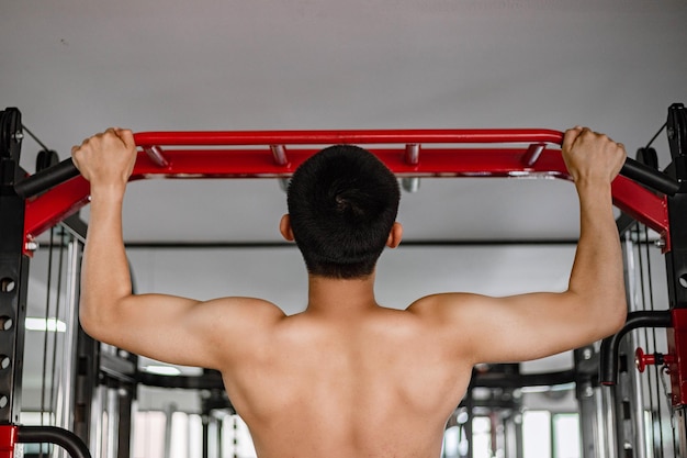 Trainingskonzept ein starker junger Erwachsener, der mit seinen beiden Händen Klimmzüge macht, die sich selbst ziehen