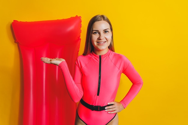 Traje de baño de una pieza rosa de cuerpo delgado de mujer joven en colchón de aire rosa aislado sobre fondo de estudio de color amarillo brillante verano hotel piscina mar vacaciones concepto de bronceado Lugar para texto