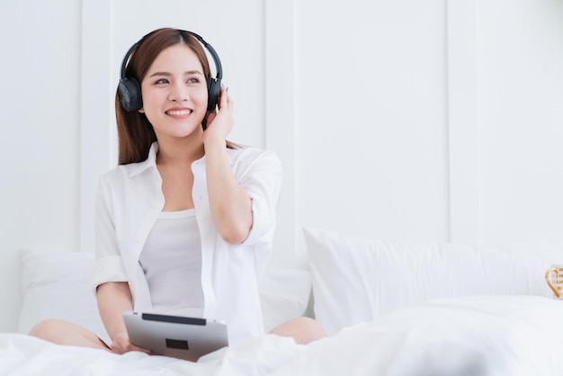 Traje de vestido branco de mulher asiática de felicidade gosta de dançar ouvindo música com fundo de quarto de fone de ouvido